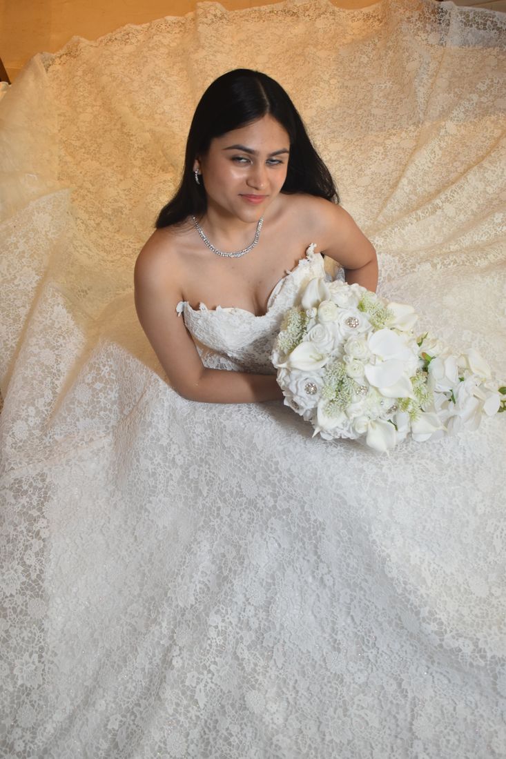 Bride seated in lace holding a cascading bouquet of white roses, calla lilies and orchids